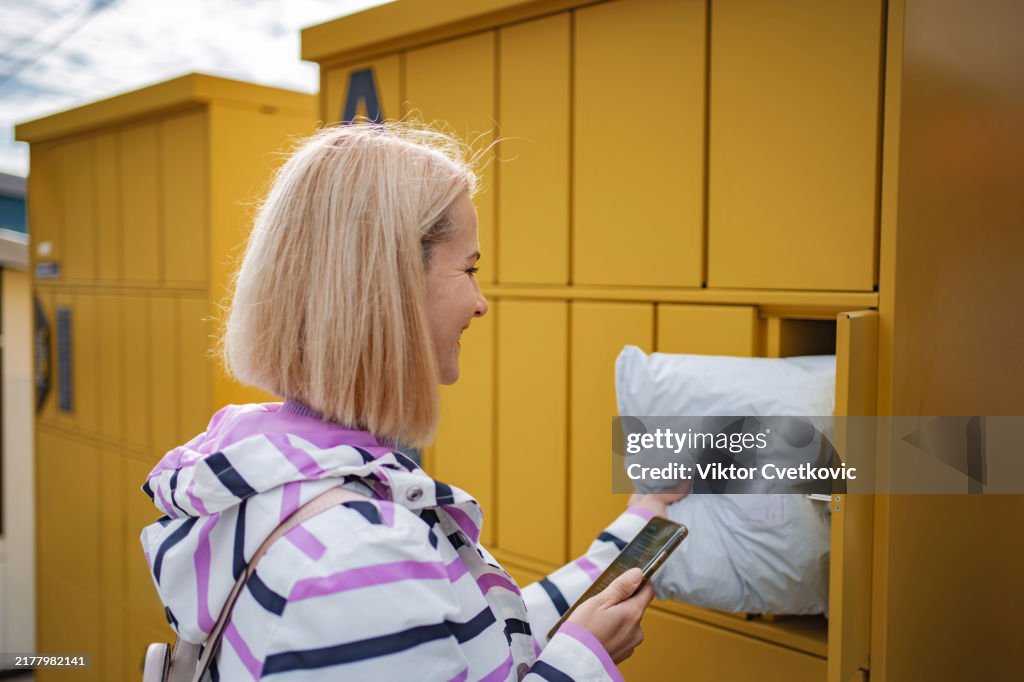 Junge erwachsene Frau, die ein Paket aus einem intelligenten elektronischen Schließfach abholt