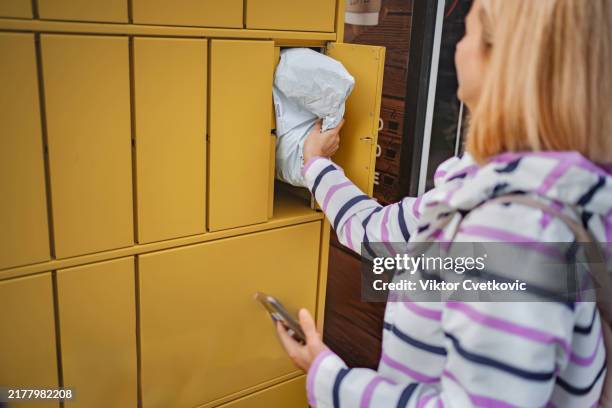 woman using smartphone to collect parcel from automated locker - parcel locker stock pictures, royalty-free photos & images
