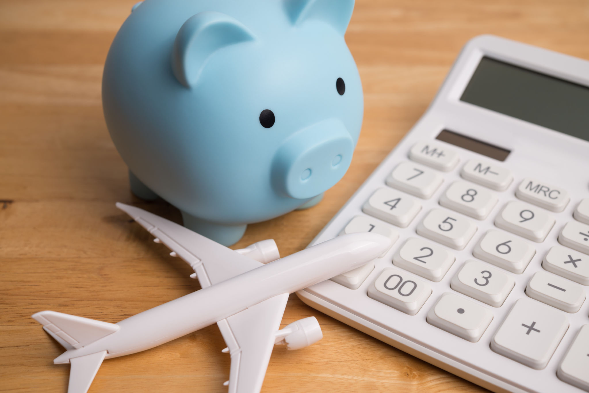 Blue piggy bank, airplane and white calculator on wooden table background. Blue piggy bank, airplane and white calculator on wooden table background.