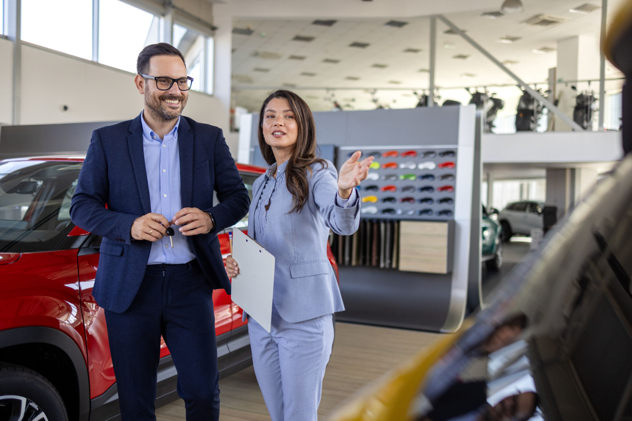 Super sales team in dealership, two consultants or managers in elegant suits with laptop and tablet in arms in car dealership Super sales team in dealership, two consultants or managers in elegant suits with laptop and tablet in arms in car dealership