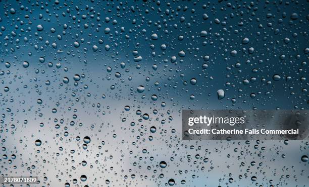 conceptual, abstract background image of raindrops on a windowpane reflecting a cloudy sky in the evening during a rain shower - lluvia fotografías e imágenes de stock