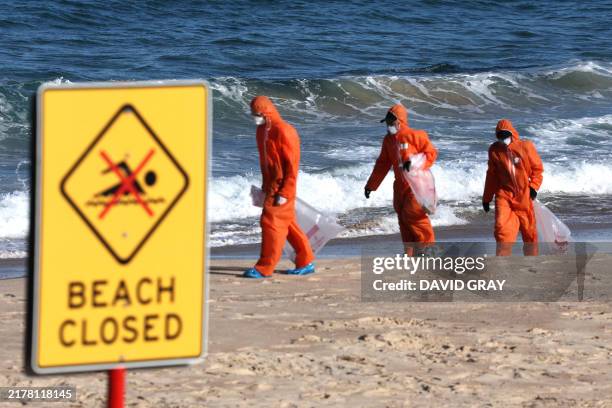 Workers in protective suits conduct a cleanup operation to clear petroleum-based "tar balls" washed ashore on Coogee Beach in Sydney on October 17,...