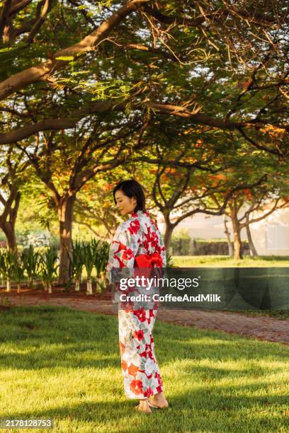titre : grâce culturelle dans le jardin ensoleillé, une femme en kimono traditionnel se promenant parmi les arbres - kimono photos et images de collection