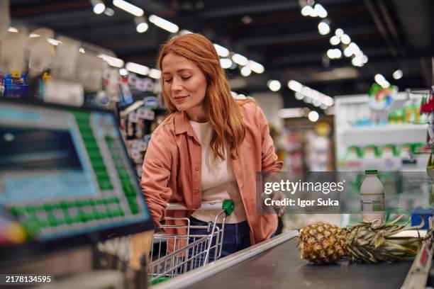 lächelnde frau, die in einem supermarkt einkaufen von lebensmitteln - einkaufskorb stock-fotos und bilder
