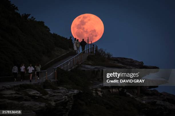 Super moon rises behind people standing on a headland near Sydney's Bondi Beach on October 17, 2024.