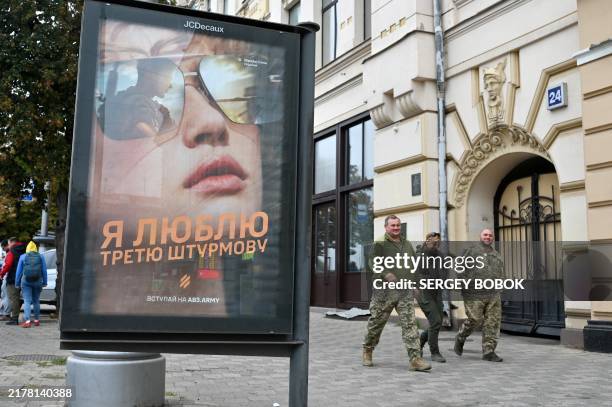 Ukrainian servicemen walk by a poster displaying a recruitment advertisement of the Third Assault Brigade in Kharkiv, on October 13 amid the Russian...