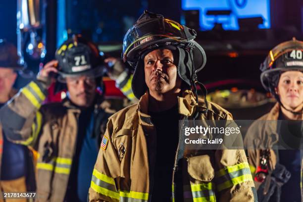 gemischtrassige gruppe von feuerwehrleuten mit feuerwehrfahrzeugen bei nacht - feuerwehrmann stock-fotos und bilder