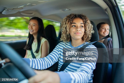Young Multiracial teenager girl driving car while Asian friend sits in car with friends passenger Young Multiracial teenager girl driving car while Asian friend sits in car with friends passenger