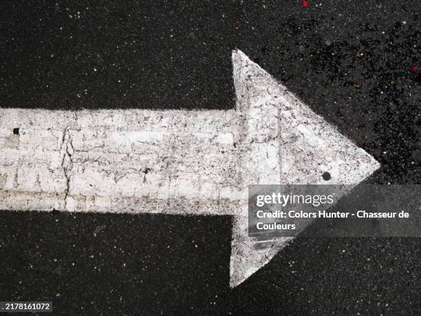 a painted and patinated white arrow on the grey asphalt of a street in london, england, united kingdom. rough texture. sunlight. natural colors. - arrow symbol stock pictures, royalty-free photos & images