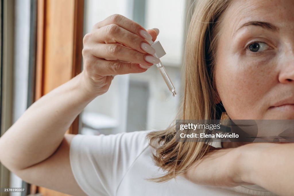 Close-up of a woman's hands with a pipette drops hair growth serum or hair oil with a dropper , hair care