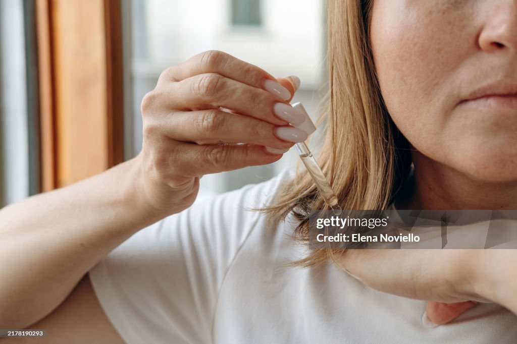 Close-up of a woman's hands with a pipette drops hair growth serum or hair oil with a dropper , hair care