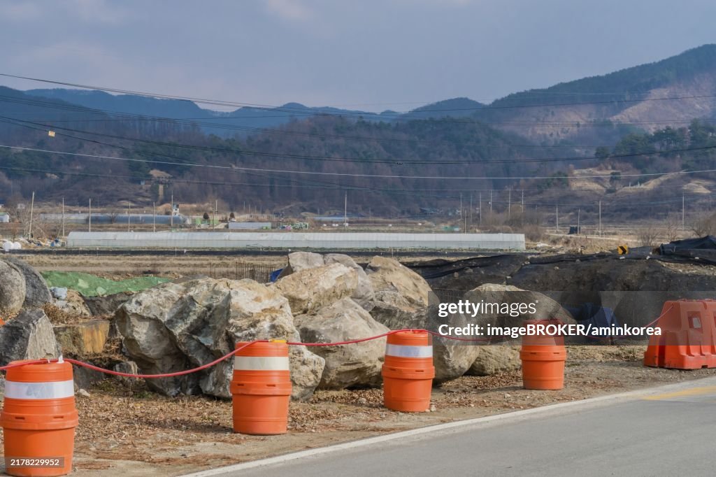 Orange traffic barrels on side of rural road in front of large boulders at construction site in South Korea