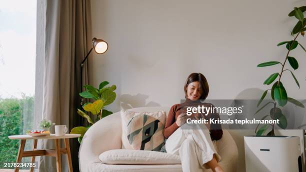 jeune femme asiatique allumant le purificateur d’air avant de lire dans le salon. - chambre bien rangée photos et images de collection