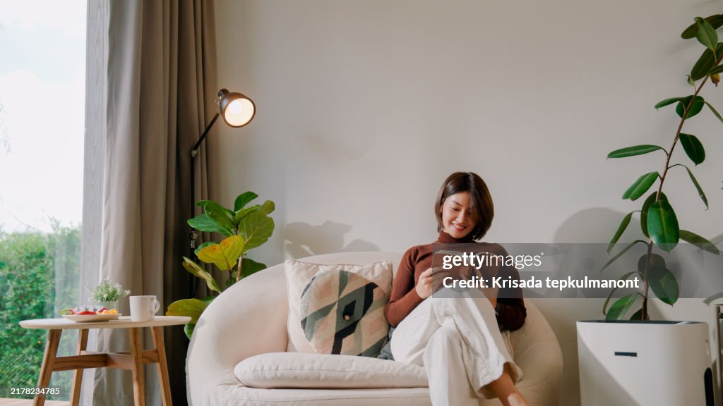 Young Asian woman turning on air purifier before reading in the living room.