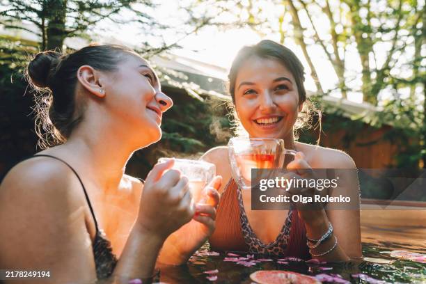herbal tea relaxation. content women drinking sea buckthorn herbal tea in hot springs during nature getaway - decolleté stockfoto's en -beelden