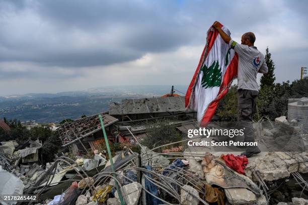 Member of the Hezbollah-affiliated civil defense force, an emergency response organization, raises the Lebanese flag amid rubble that remains from an...