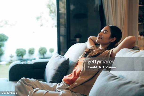 gen z woman relaxing on couch, enjoying fresh air from open door - ontgiften stockfoto's en -beelden