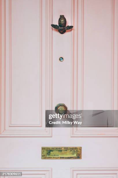 pastel pink door featuring ornate brass hardware, including a bee-shaped knocker and an aged letterbox. - doorknob stock pictures, royalty-free photos & images