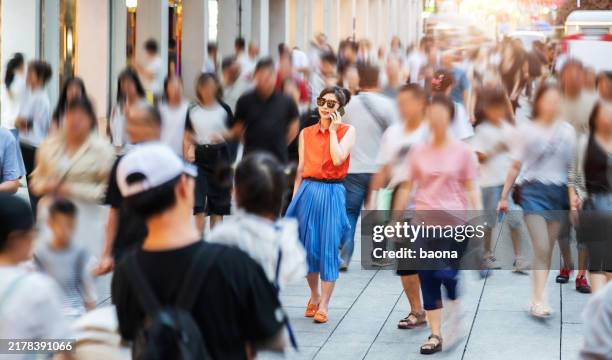 modische frau, die ein smartphone benutzt und auf einer belebten straße geht - menschenmenge stock-fotos und bilder