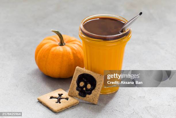 pumpkin smoothie with coffee in a glass with a drinking straw. with spicy square cookies with black marmalade filling in the shape of a skull and bones. light grey background - red heart shaped glasses stock pictures, royalty-free photos & images