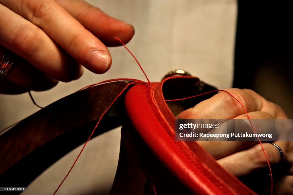 Craftswoman in a workshop attaches a shoulder belt to a ready-made handmade leather briefcase