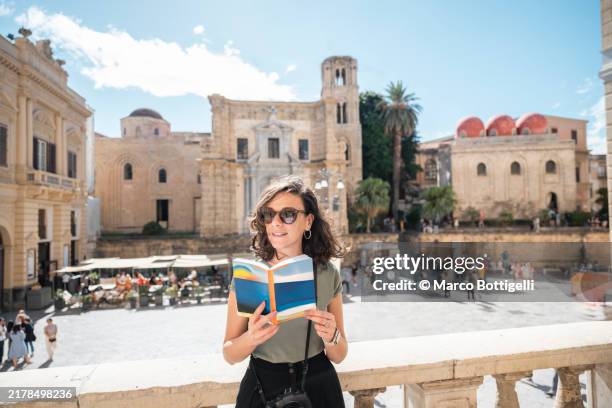 young cheerful woman reading a guidebook in palermo, sicily, italy - guidebook stock pictures, royalty-free photos & images