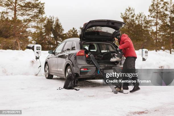 a man unpacking ski equipment from his electric car, at a charging station. - esqui e snowboard imagens e fotografias de stock