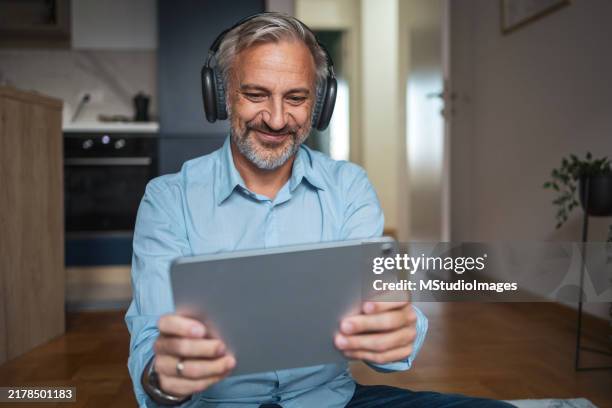 hombre maduro que usa tableta y auriculares en casa para relajarse - hombres de mediana edad fotografías e imágenes de stock