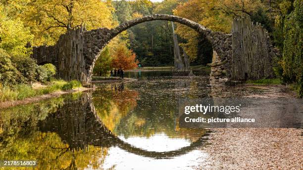 October 2024, Saxony, Kromlau: The Rakotzbrücke bridge in Kromlau Rhododendron Park is reflected in the Rakotzsee lake. The basalt stone bridge in...