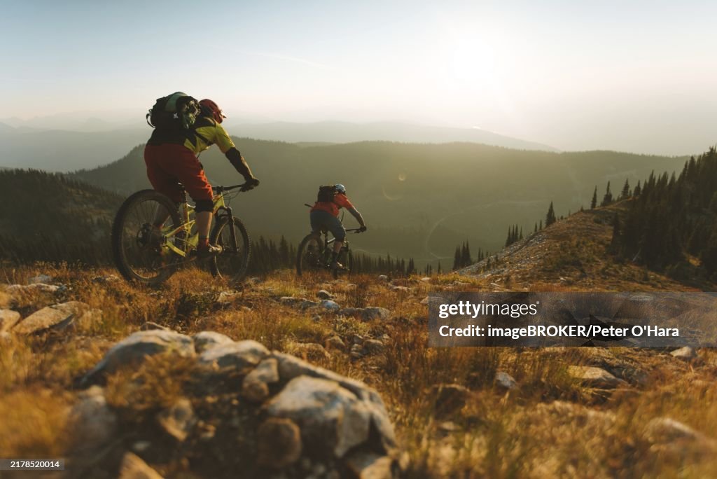 Mountain Bikers Descending A Trail During Sunrise With Hills And A