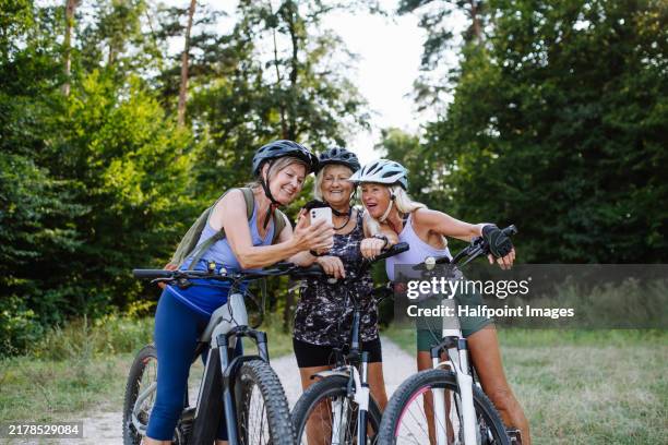 three senior friends on bike tour in nature taking selfie. older women on low impact route riding electric bikes. - incontinence stock pictures, royalty-free photos & images