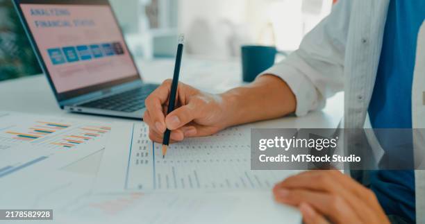 closeup of young asian man working from home, writing notes and analyzing financial data, showcasing remote work and financial planning. remotely and finance. - financial planning stock pictures, royalty-free photos & images