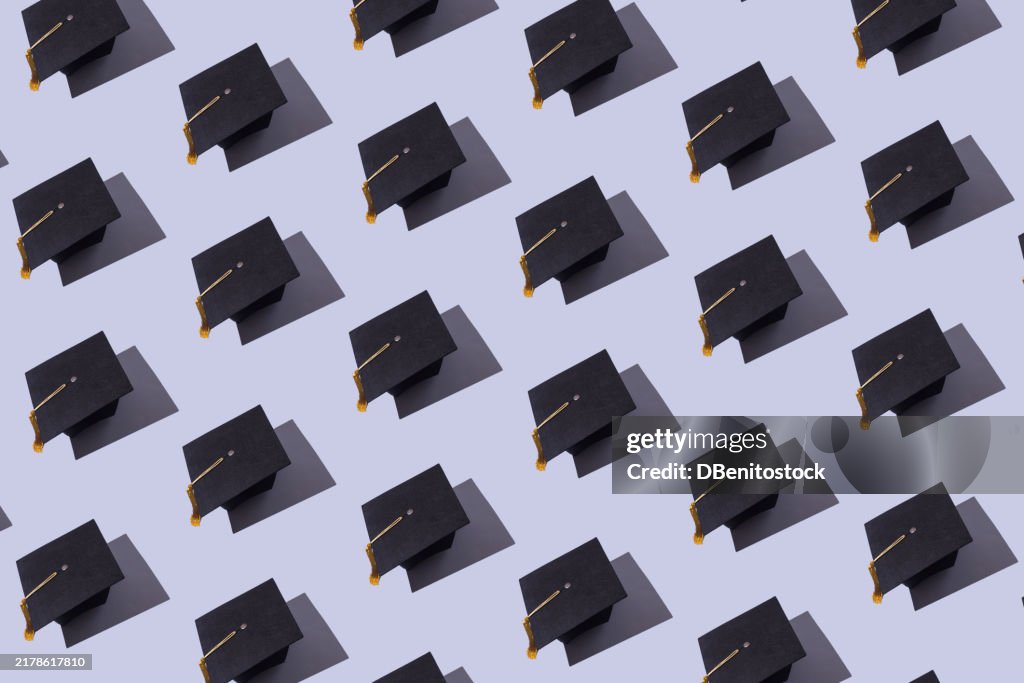 Pattern of black graduation caps with gold tassel with hard shadow, on blue pastel background. Graduation, achievement, goal, degree, master's, bachelor's, university, college and success