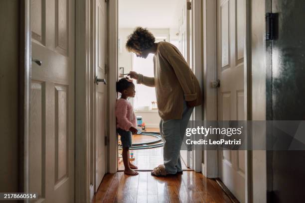 mother measuring daughter's height and marking on wall at home - altezza umana foto e immagini stock