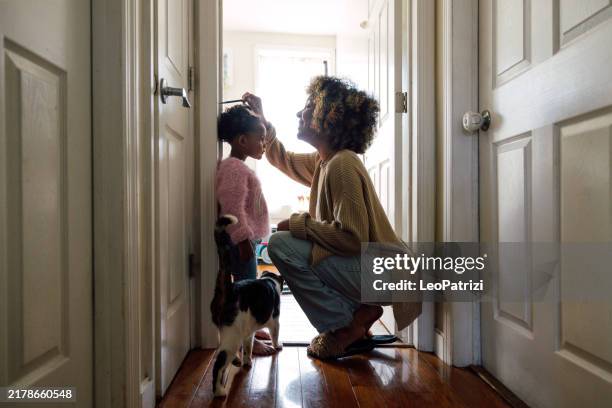 mother measuring daughter's height and marking on wall at home - cat high up stock pictures, royalty-free photos & images