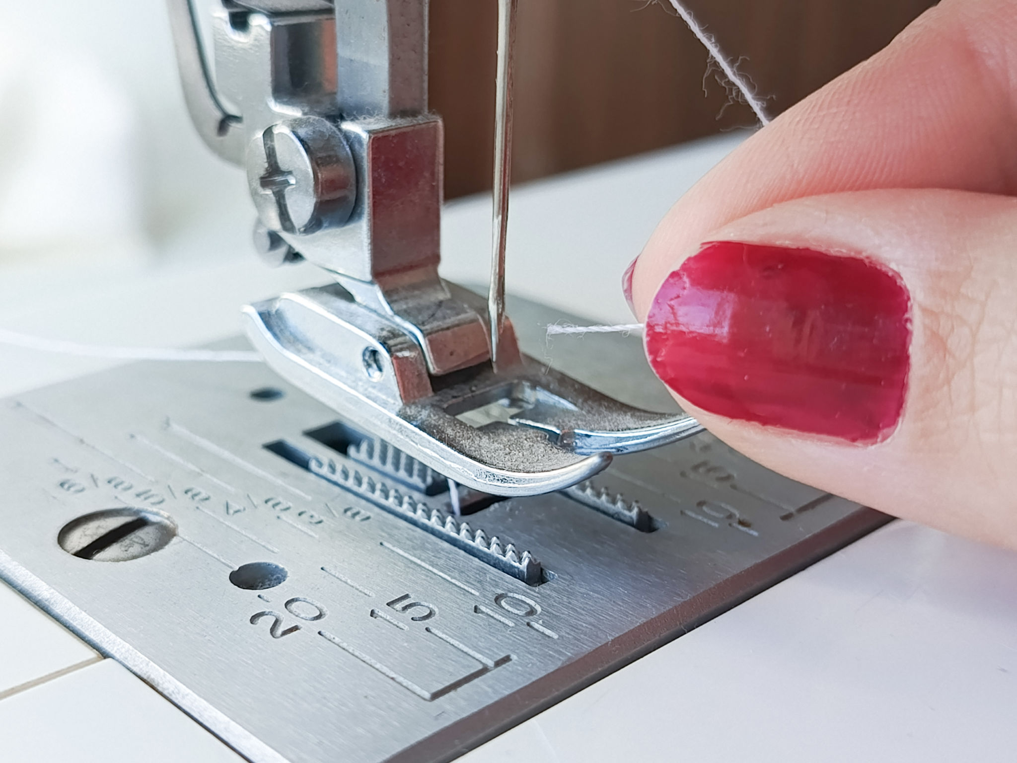 A woman threads a sewing machine needle. Sewing needle and foot in a sewing machine. Sewing production. Advertising background, space for text. Atelier. A woman threads a sewing machine needle. Sewing needle and foot in a sewing machine. Sewing production. Advertising background, space for text. Atelier.