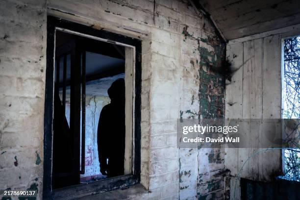a creepy horror concept. inside a ruined abandoned house. with a spooky dark hooded figure silhouetted through a window - ugly house photos stock pictures, royalty-free photos & images
