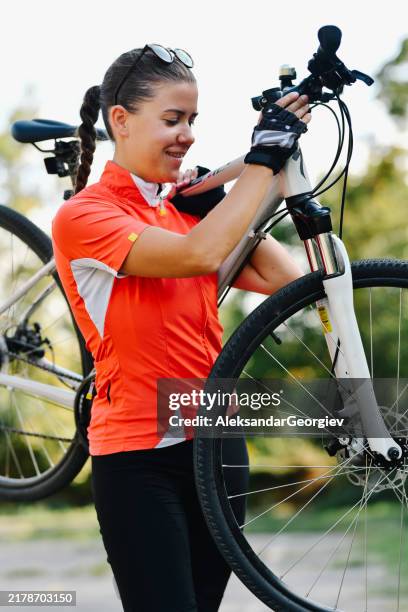 strong female biker effortlessly carrying bike on shoulder smiling and getting ready for biking event - cycling shorts stock pictures, royalty-free photos & images