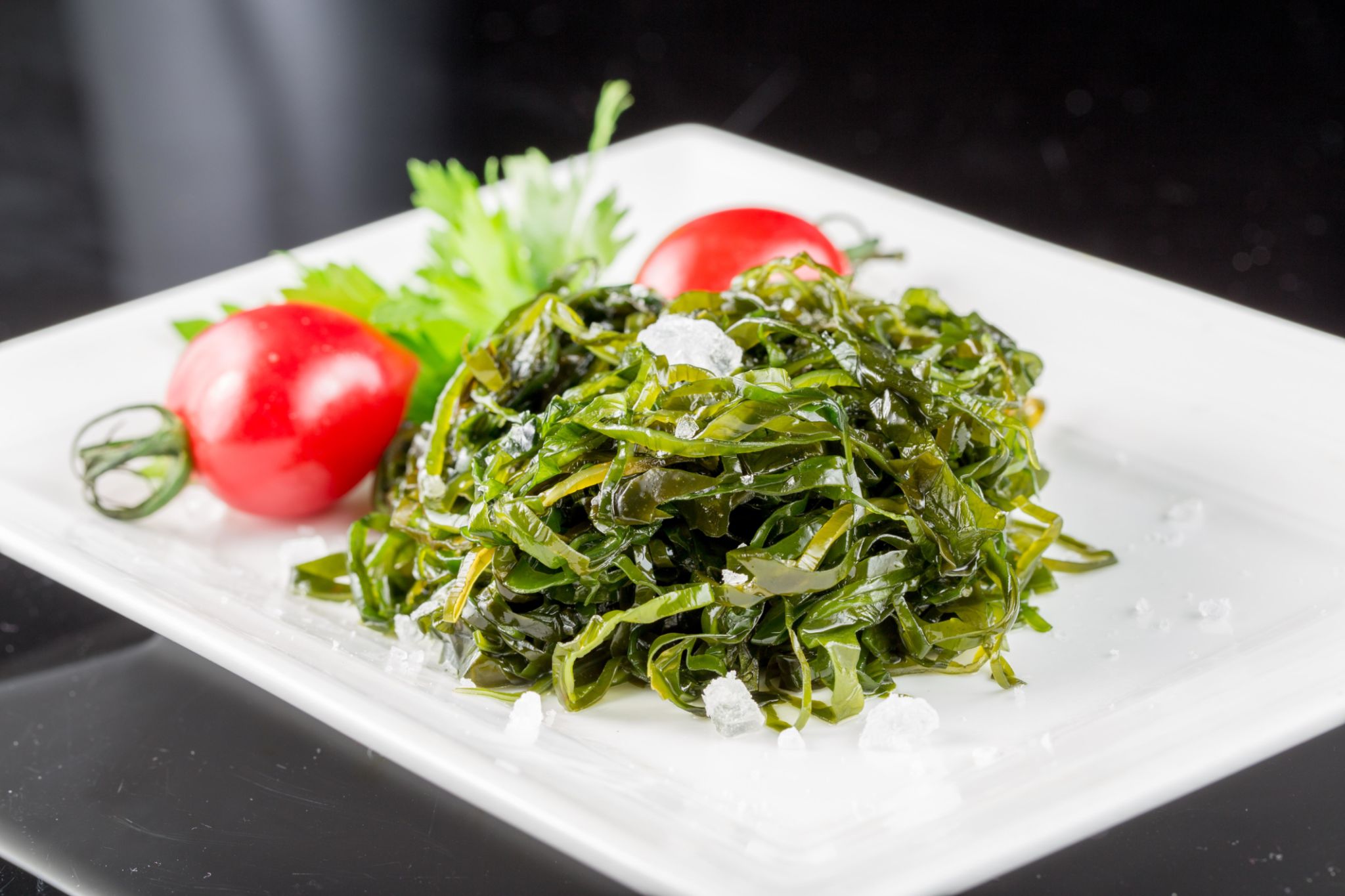 A plate of seaweed salad with cherry tomatoes and parsley A plate of seaweed salad with cherry tomatoes and parsley