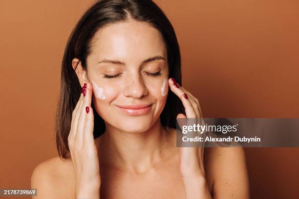 beauty portrait close up of beautiful woman applying face cream on brown background studio shot. concept sale of cream - gezichtscrème stockfoto's en -beelden