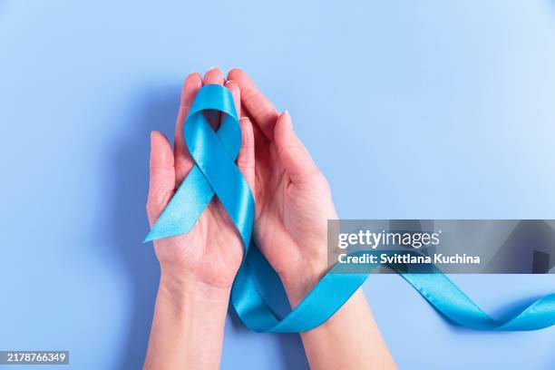 colorectal cancer ribbon in female hands on blue background - colorectal cancer stock pictures, royalty-free photos & images