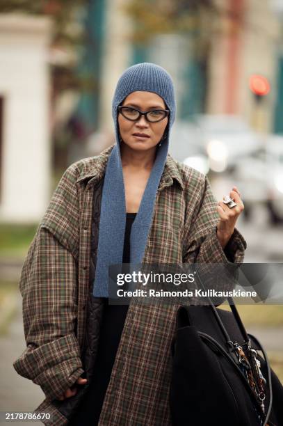 Guest wears brown checkered coat, black oversized bag with accessories and blue hat during the 10th season of the Visa Fashion Week Almaty on October...