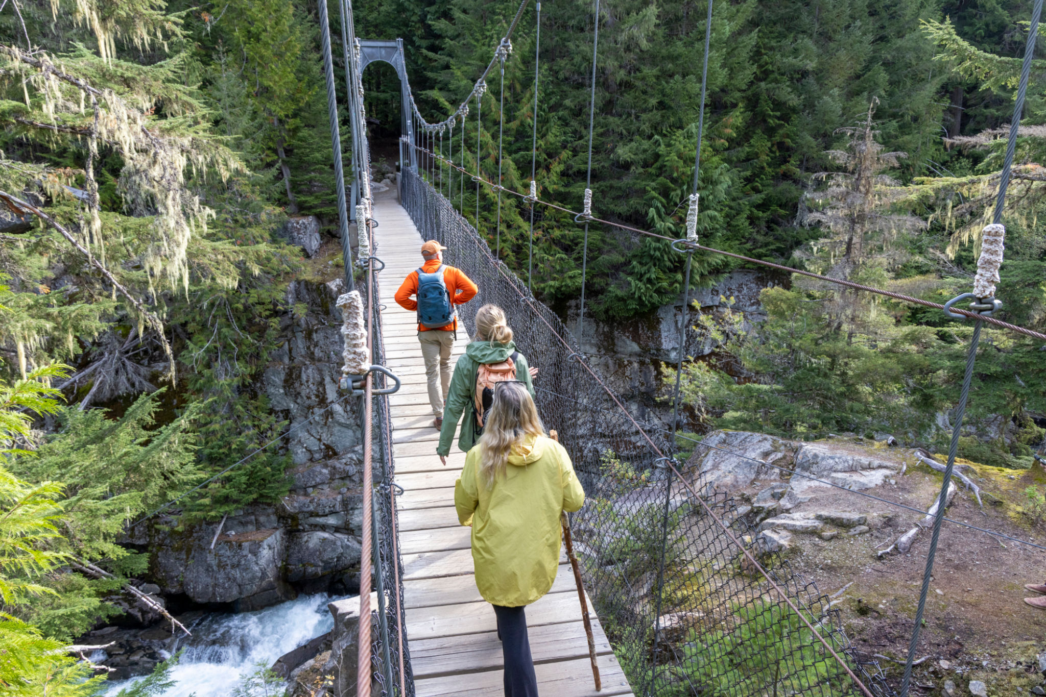 Guide and guests hike across suspension bridge over river Guide and guests hike across suspension bridge over river