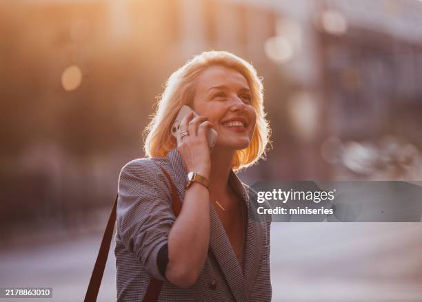 confident businesswoman enjoying a phone call on the city street - warm light stock pictures, royalty-free photos & images