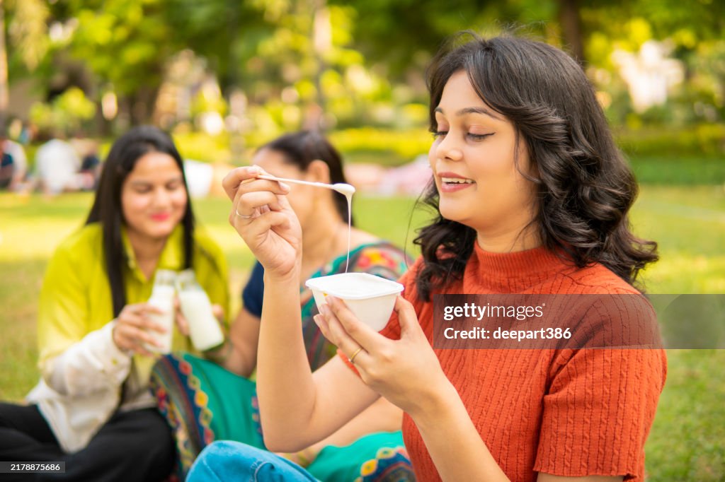 Happy indian family enjoying a picnic and eating a variety of dairy products in the park
