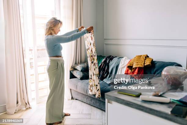 mid adult woman organizing wardrobe and trying on clothes at home - decluttering stock pictures, royalty-free photos & images
