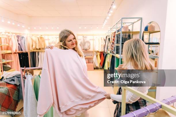 two mid adult women shopping in a boutique store shop exploring clothing options. - modestylistin stock-fotos und bilder