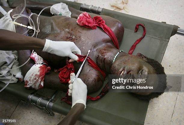 Doctor cuts off the bloody shirt of a government soldier who was injured in fighting at JFK Hospital July 20, 2003 in Monrovia, Liberia. Government...