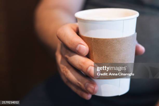 a person holding a takeaway coffee cup in hand with a cardboard sleeve, captured in a cozy indoor setting during the morning - ärmel stock-fotos und bilder
