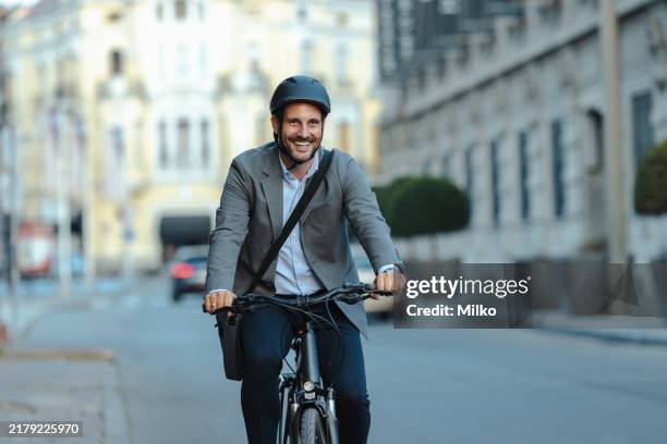 hombre de negocios sonriente seguro que viaja en bicicleta en la calle de la ciudad - ciclista fotografías e imágenes de stock